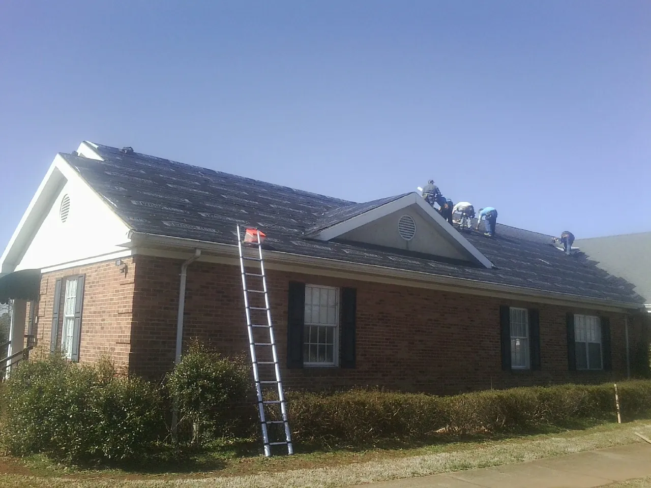 Crew tearing shingles off a brick ranch roof with a ladder set — Metal Roof Repair work by our crew in Whitehouse