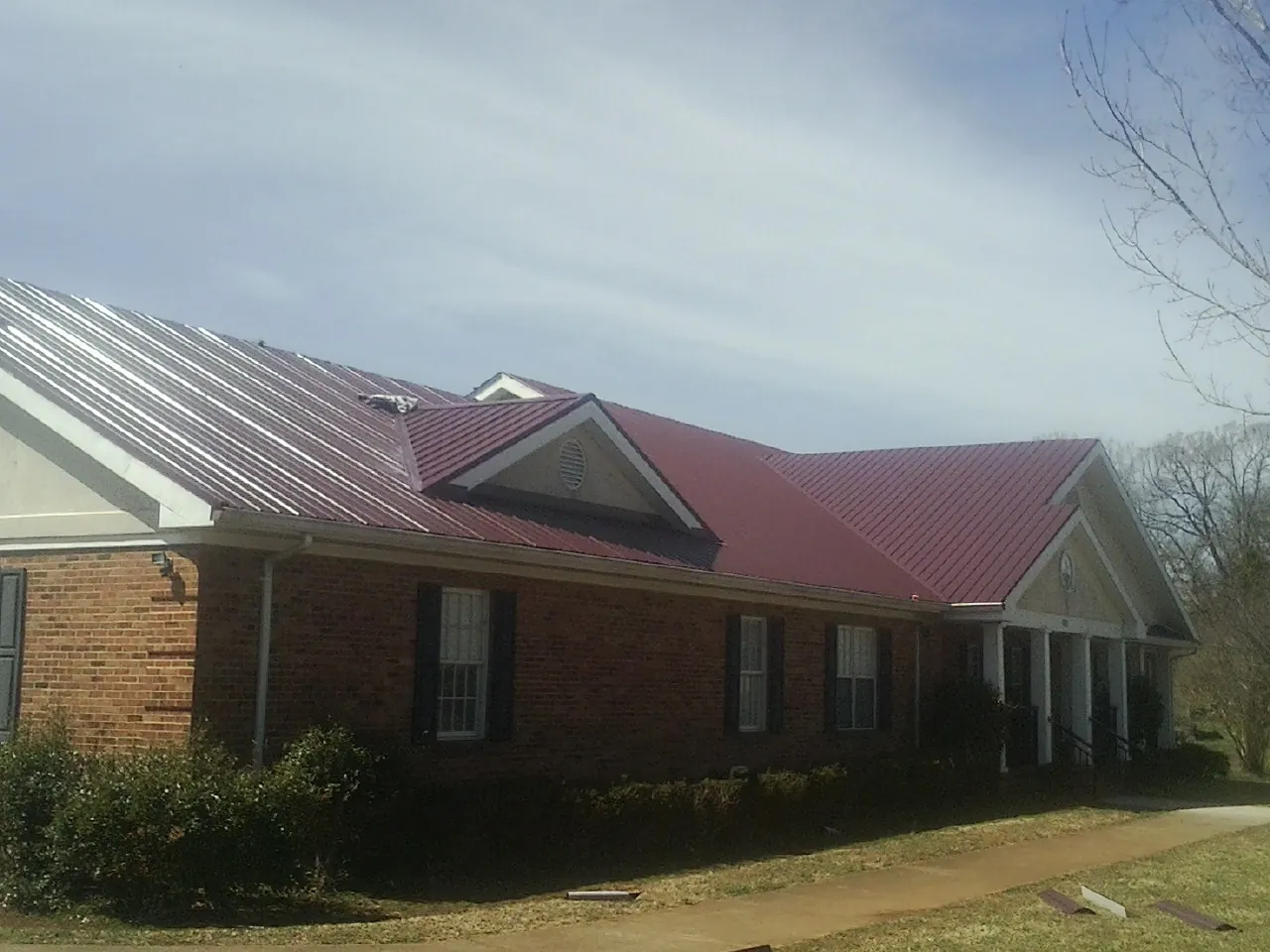 Red metal roof with gabled entries on a long brick building, from a Hail Damage Roof Repair job in Whitehouse